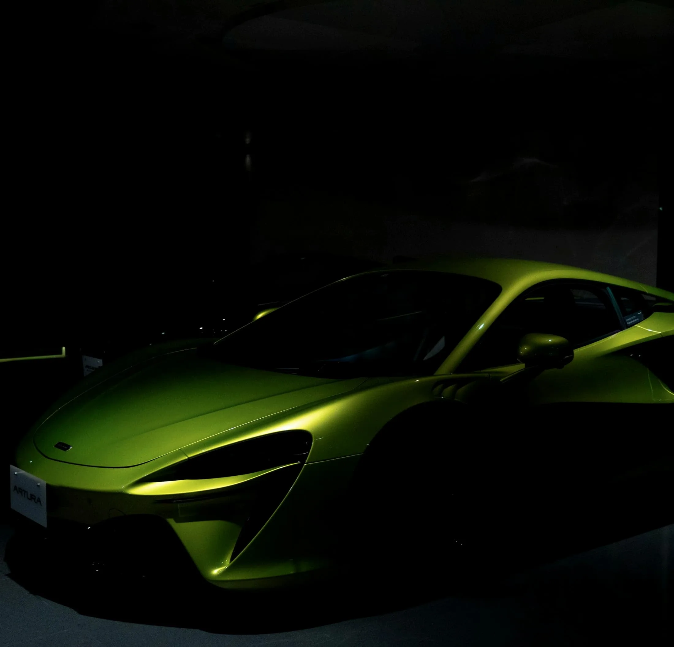 Metallic green McLaren Artura lit from the side in a black room