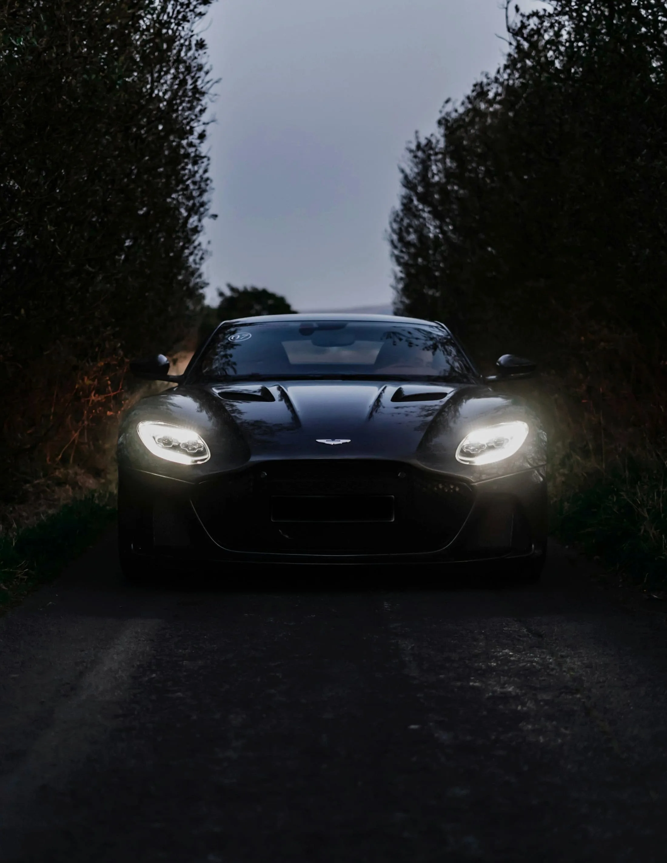 Aston Martin DBS Superleggera head-on at dusk, headlights on