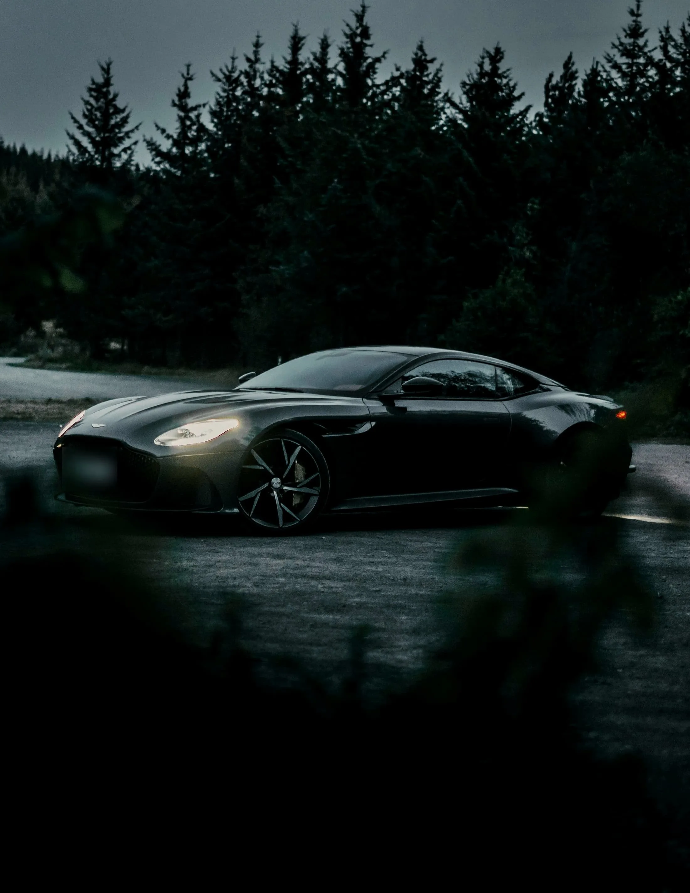 Aston Martin DBS Superleggera in near darkness, one headlight burning