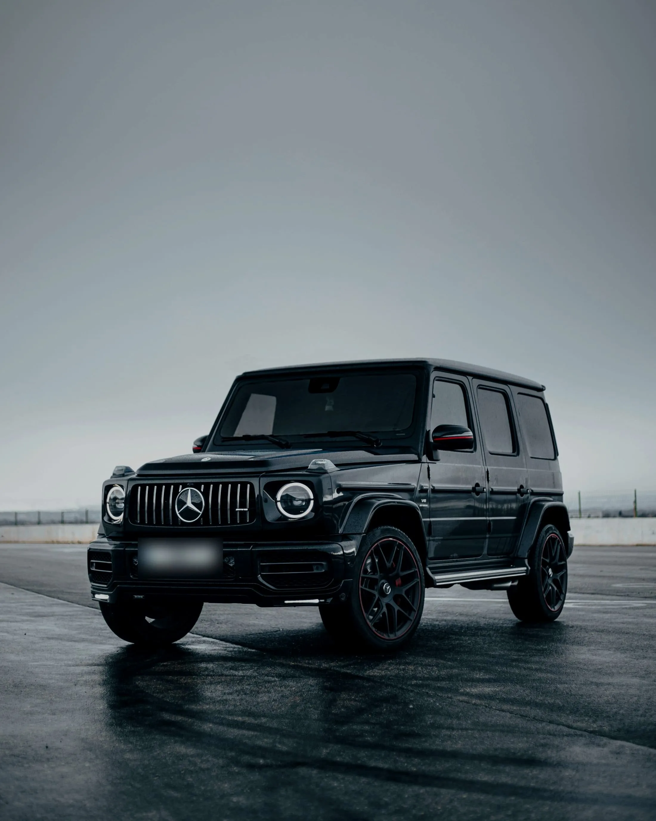 Black Mercedes-AMG G 63 on wet concrete under a pale sky