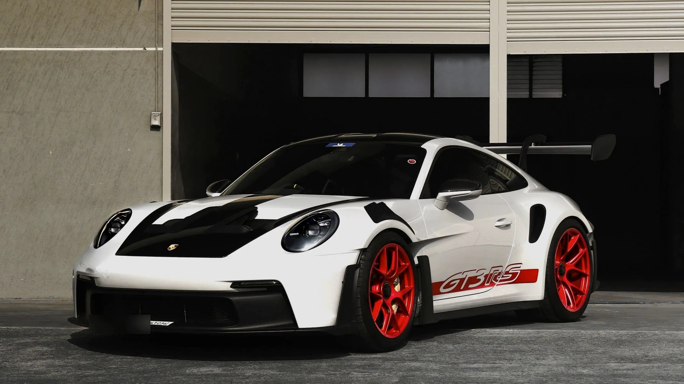 White Porsche 911 GT3 RS with black bonnet and red wheels in front of a dark doorway