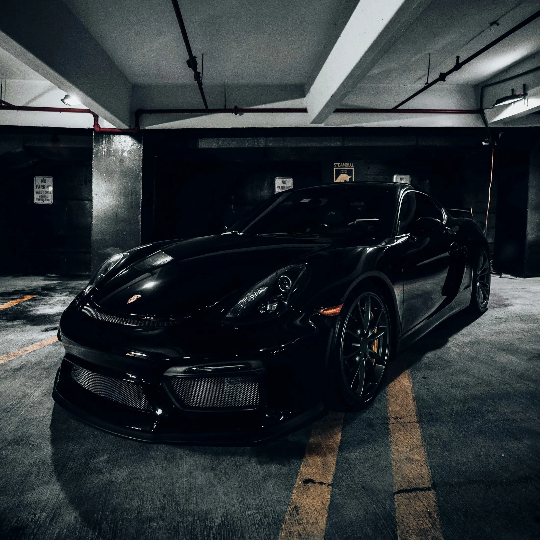 Black Porsche 718 Cayman GT4 in an underground car park, bonnet glossed by overhead light