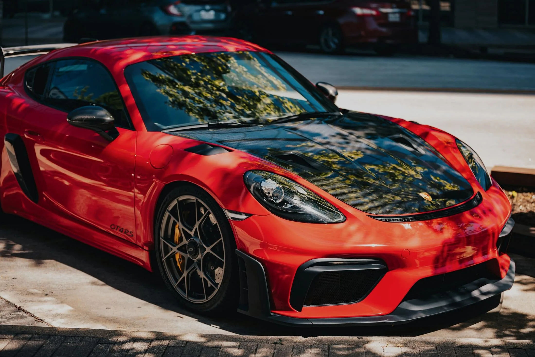 Red Porsche 718 Cayman GT4 RS with a carbon bonnet reflecting trees