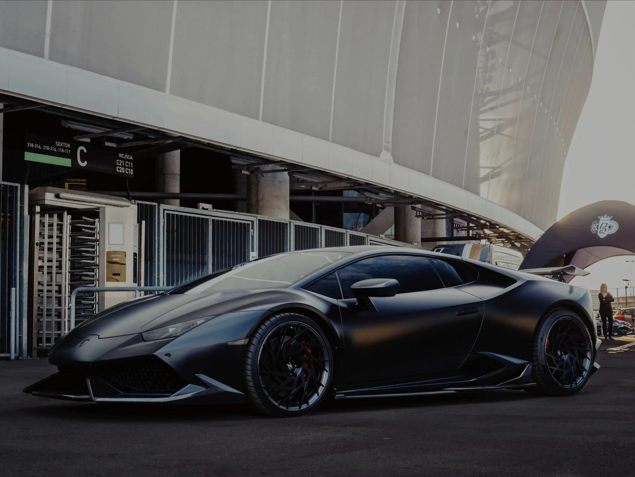 Matte black Lamborghini Huracán in profile outside a stadium