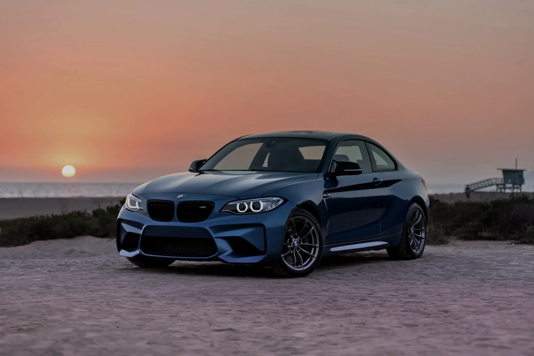 Blue BMW M2 Competition on a beach track with the sun low behind it