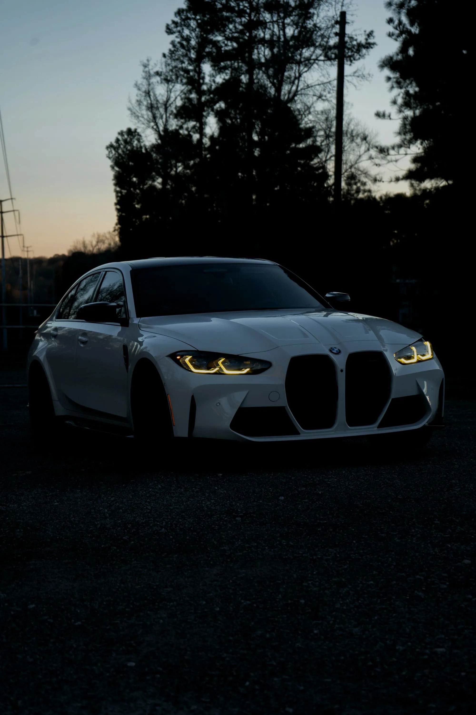 White BMW M3 Competition low and head-on at dusk, angel eyes in amber