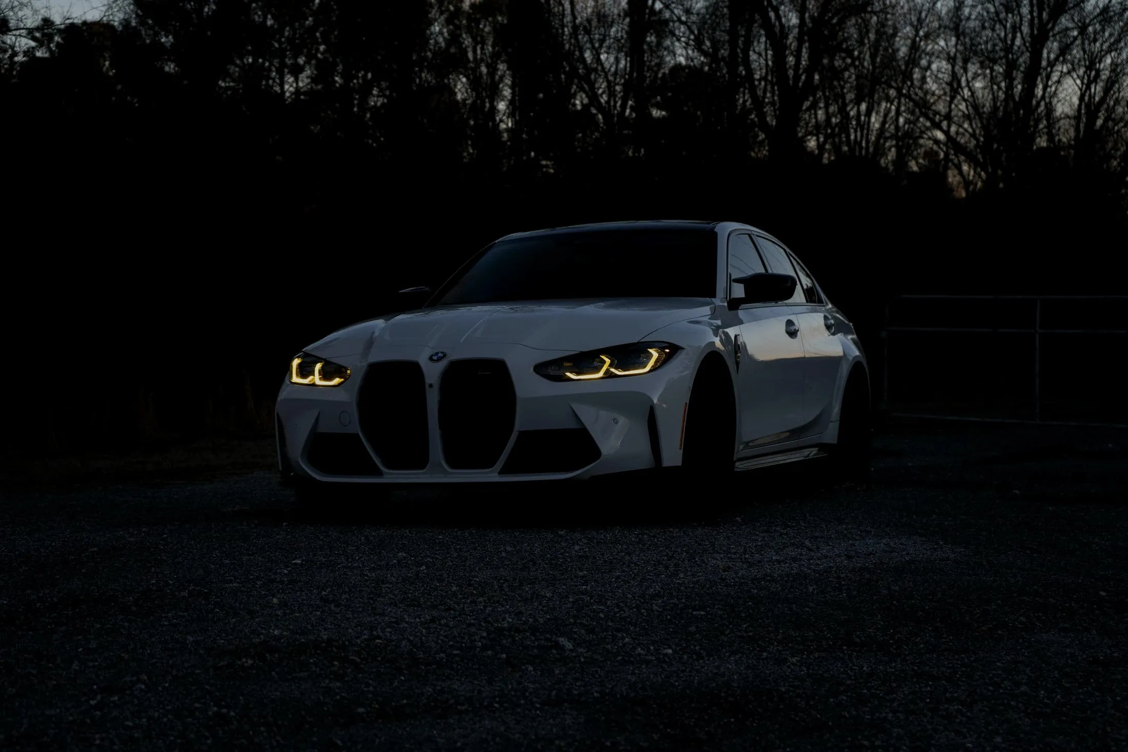 White BMW M3 Competition alone in a dark gravel clearing