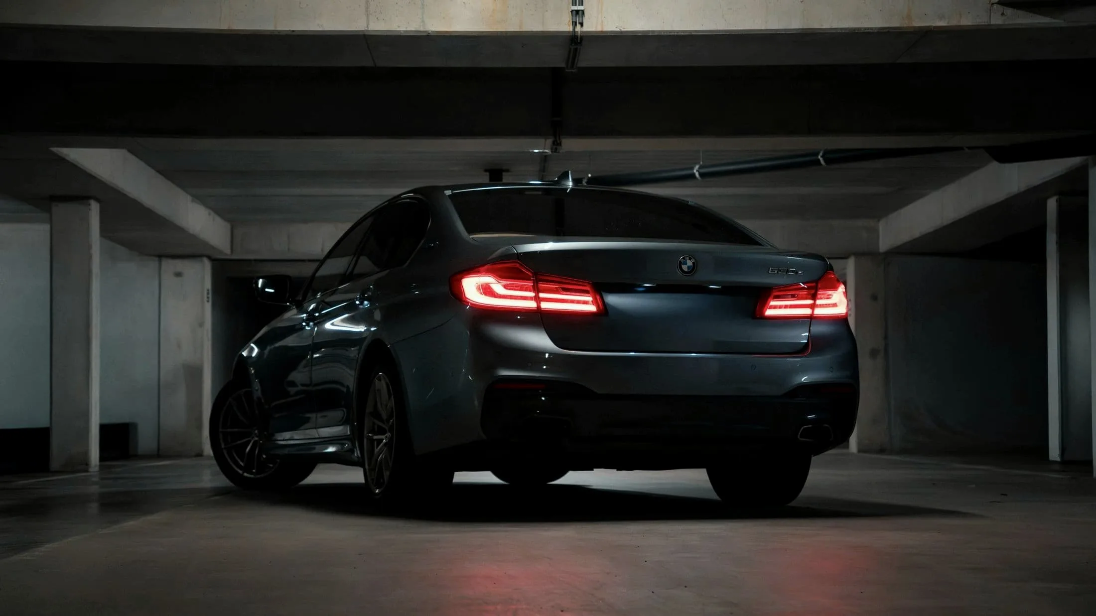 Grey BMW M5 Competition parked between concrete walls, seen from low behind