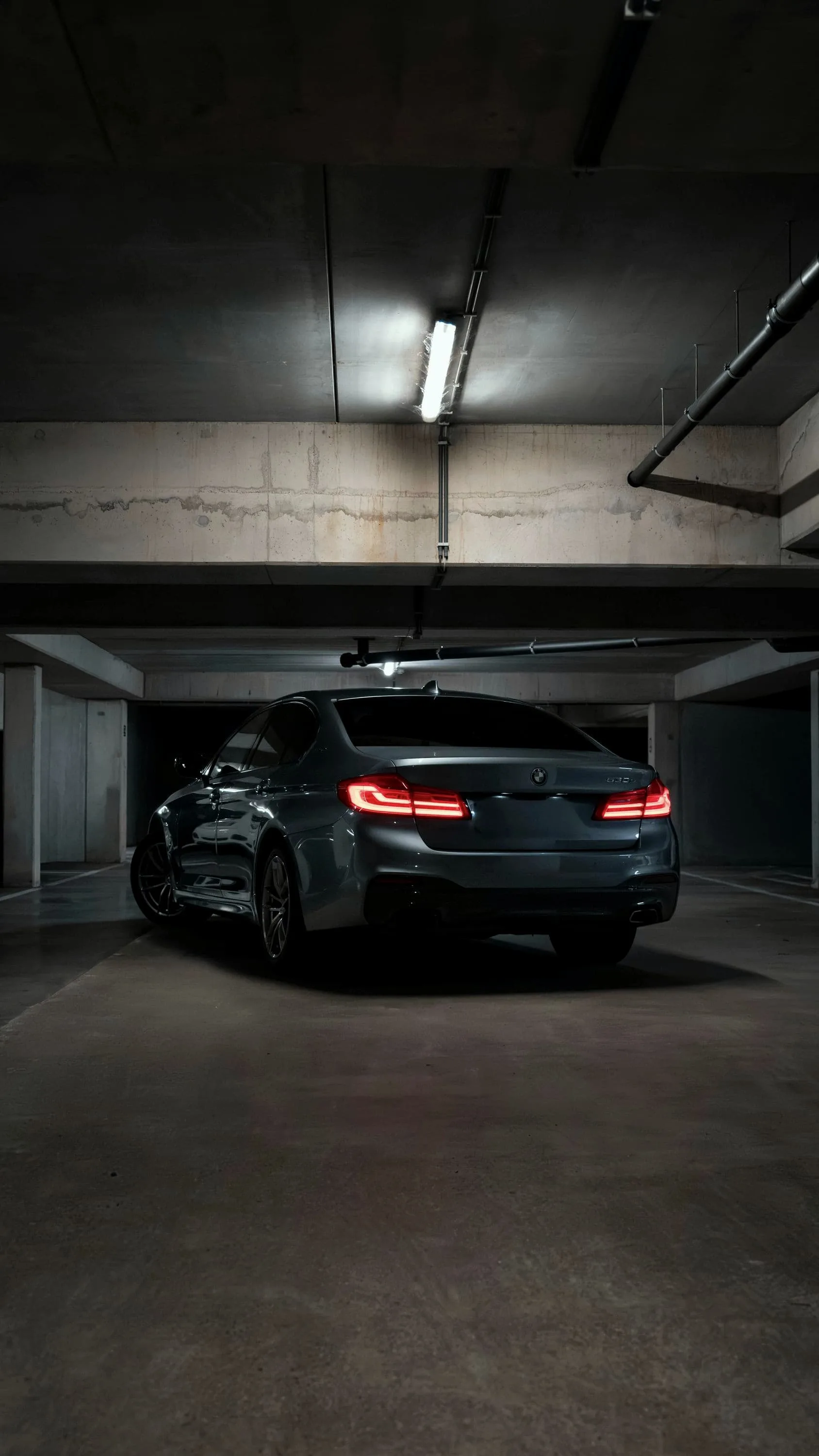 Grey BMW M5 Competition from behind in an underground garage, tail lights on
