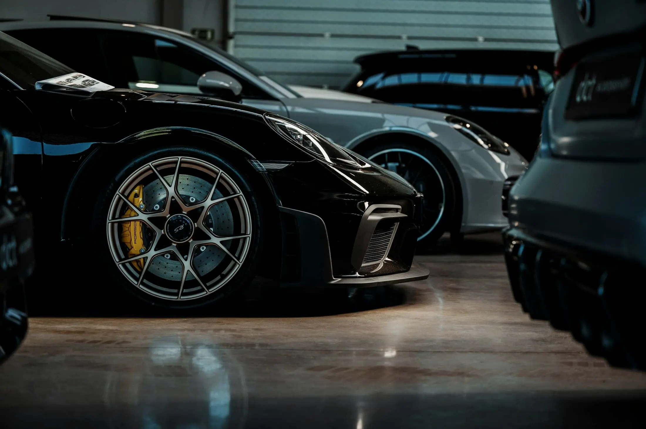 Black Porsche with gold wheels beside other cars in a low-lit service bay