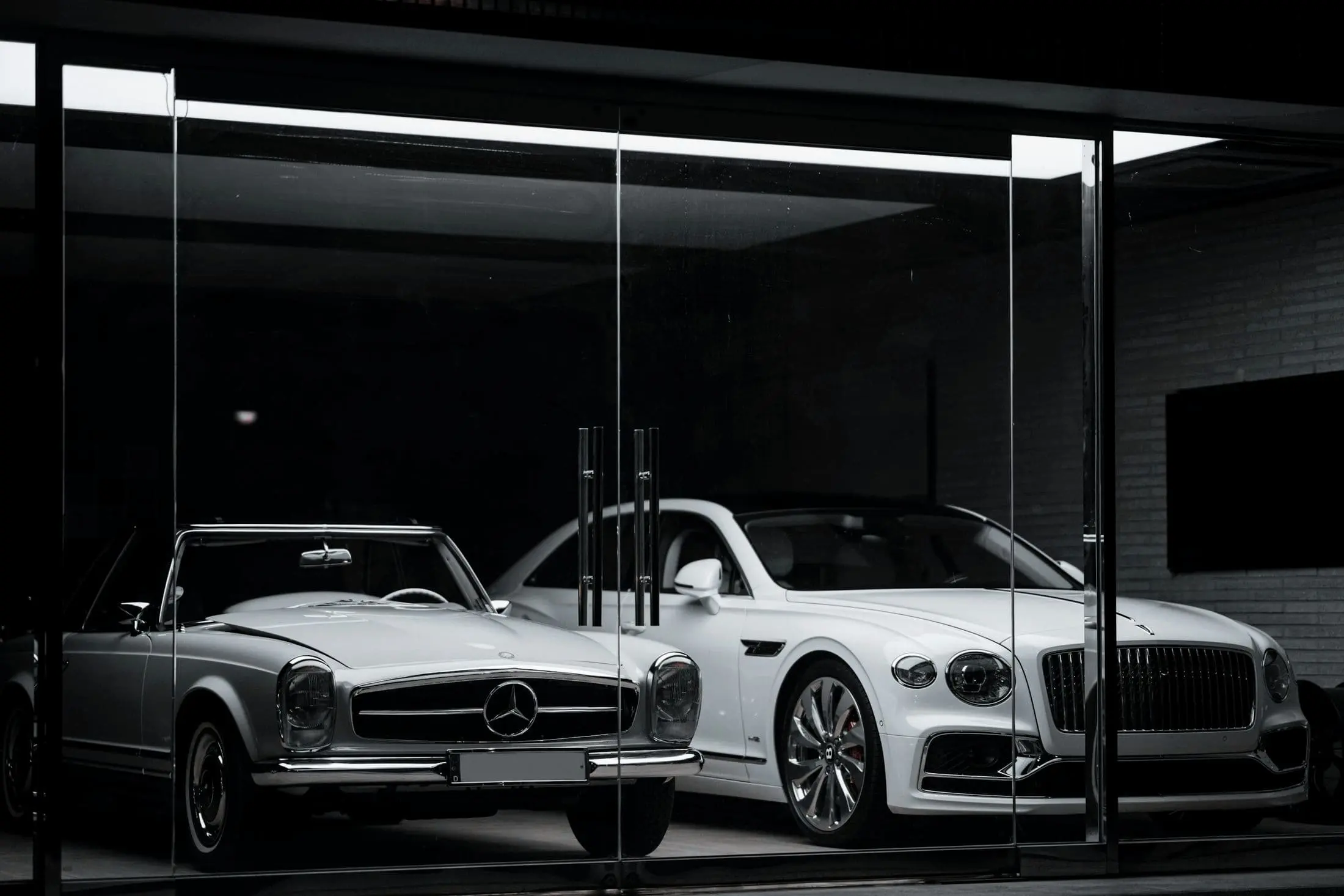 Classic Mercedes and a white Bentley presented inside a dark glass room
