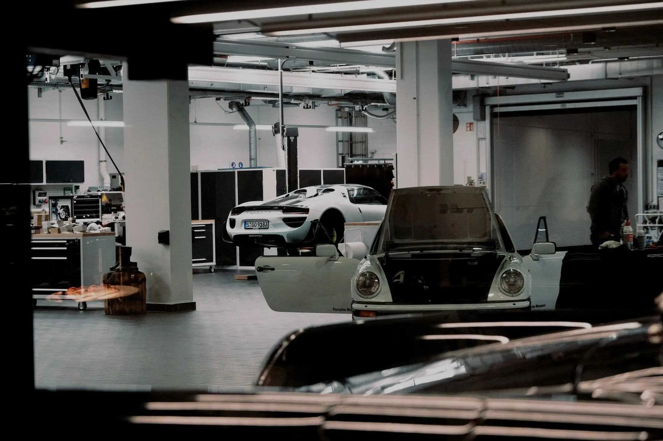 Workshop interior with a white hypercar on a lift, seen across a car with its doors open
