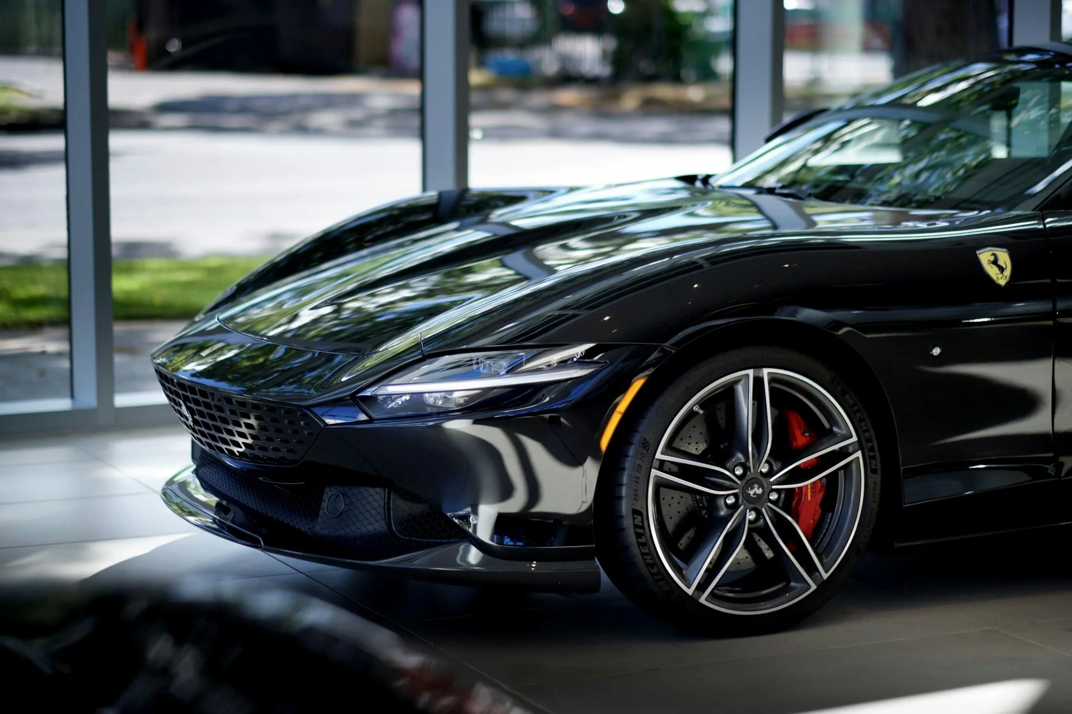 Black Ferrari Roma front three-quarter with a window wall behind