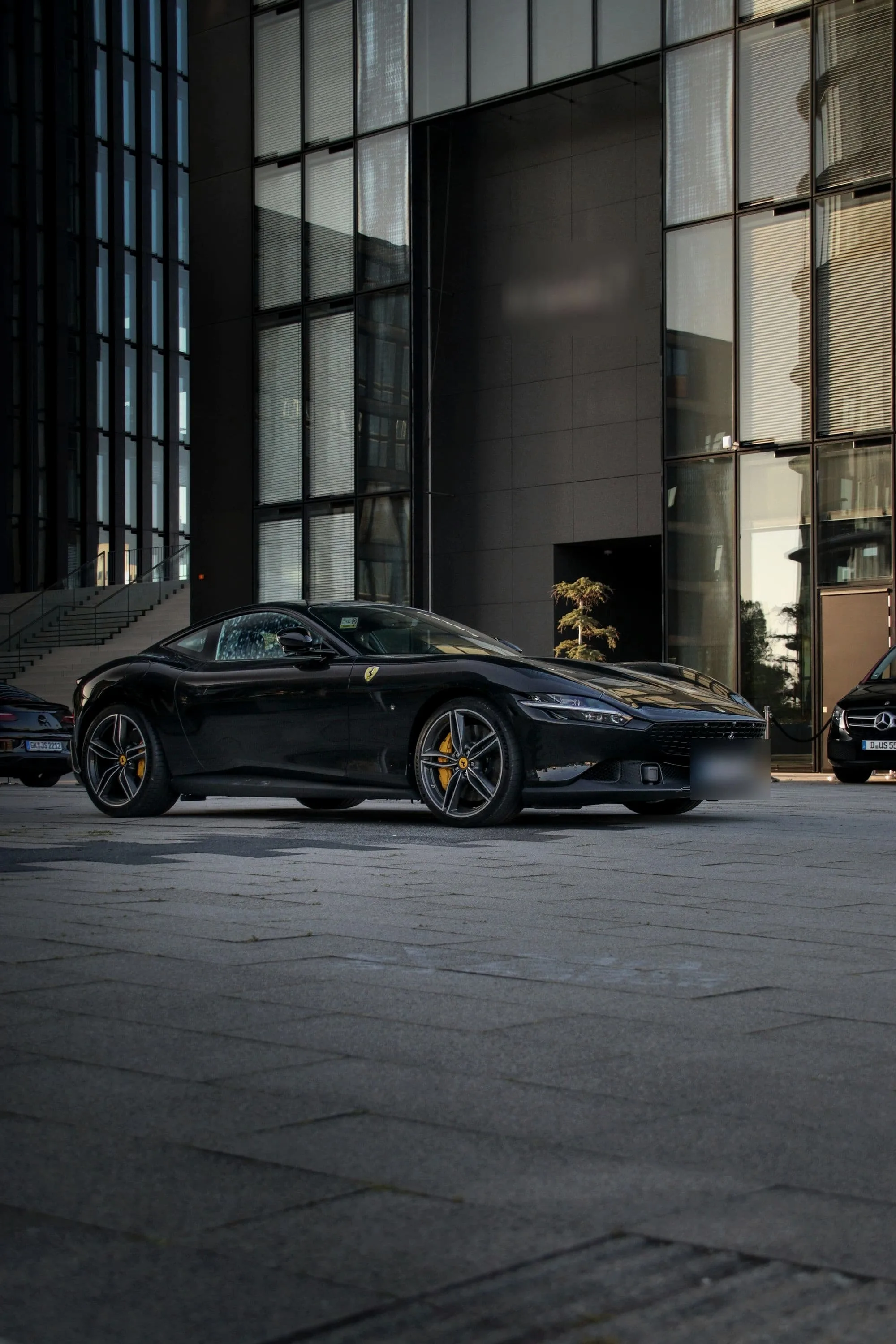 Black Ferrari Roma in profile before a dark glass building