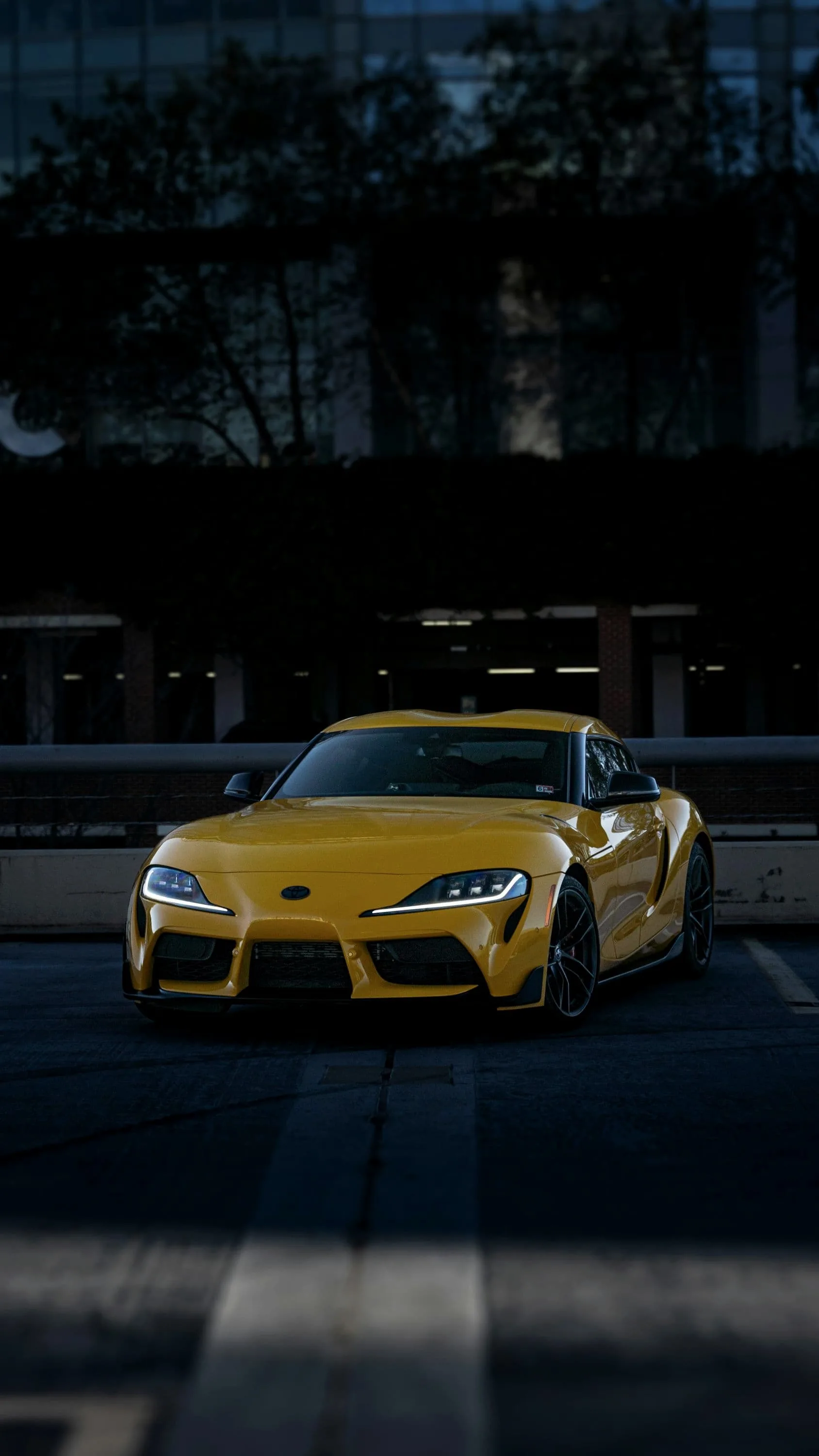 Yellow Toyota GR Supra low and head-on in front of a dark building